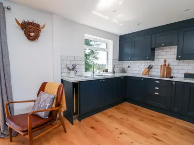 a kitchen with blue cabinets and a chair and a window at Owl Cottage in Llandrindod Wells