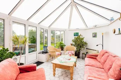 a conservatory with red couches and a table at Mid-Wales Farmhouse, swimming pool, tranquil countryside views, sleeps 14 in Meifod