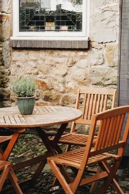 a wooden picnic table and two chairs and a window at Courtyard Cottage in Oswestry