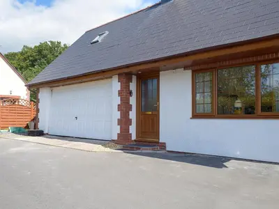 a white house with a brown roof and a garage at Windhover in Glasbury