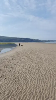 a person walking on a sandy beach near the water at Hendre Coed Isaf static caravan Barmouth in Barmouth