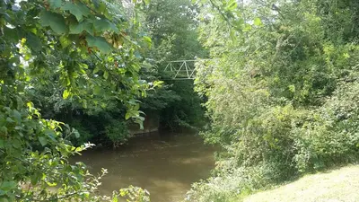 a river with a bridge in the middle of trees at The Snicketts in Ludlow