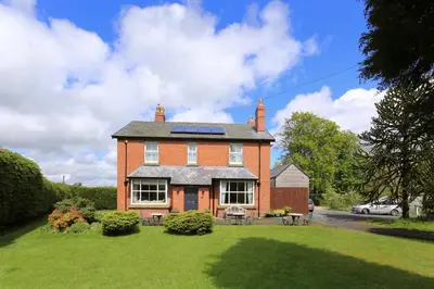 a large brick house with a lawn in front of it at The Old Vicarage Dolfor in Newtown