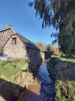 a stream next to a brick building and a house at Penybont Barn in Llangorse
