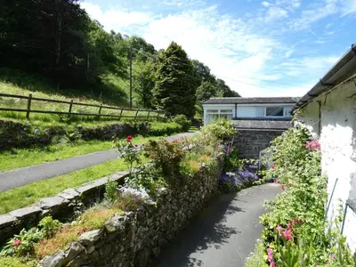 a garden with flowers next to a stone wall at Abergwynant Farm Glamping & Apartments in Dolgellau