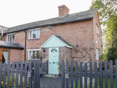 a brick house with a white door and a fence at Ensdon Lea Cottage in Shrewsbury