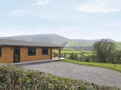 a house with mountains in the background at Bryn Eiddon Log Cabin in Machynlleth