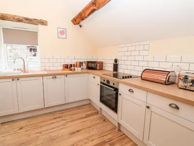 a kitchen with white cabinets and a wooden floor at Stabl, Plas Moelfre Hall Barns in Oswestry