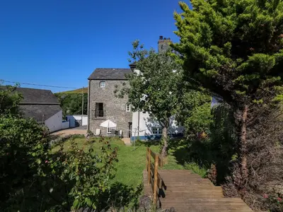 an old stone house with a wooden path leading to it at Dewi Villa in Aberaeron