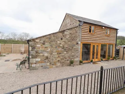 a stone barn with a fence in front of it at The Old Cart House in Oswestry
