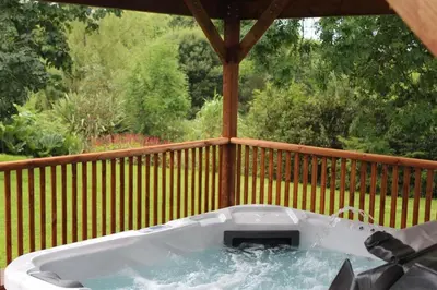 a hot tub sitting on a porch with a wooden deck at Pond Cottage in New Quay
