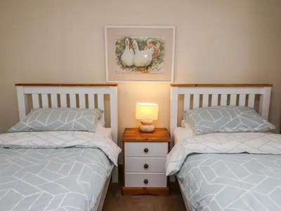 a bedroom with two beds and a night stand with a lamp at Trawsnant Cottage in New Quay