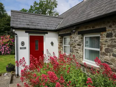 a red door on a stone house with flowers at Trawsnant Cottage in New Quay