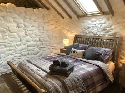 a bedroom with a bed with a stone wall at Gellibant Cottage in Llanbedr
