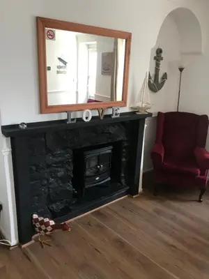 a living room with a fireplace with a mirror and a chair at Aelfor Cozy Cottage in Barmouth