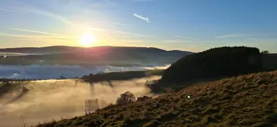 a view of a foggy field with the sun in the background at pen-rhos luxury glamping 