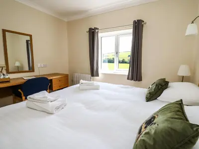 two beds in a room with a desk and a window at Llety Ceiro in Bow Street