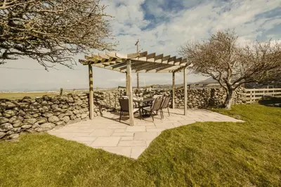 a table and chairs sitting under a wooden pergola at Bennar Isa Cottages Dyffryn Ardudwy in Barmouth