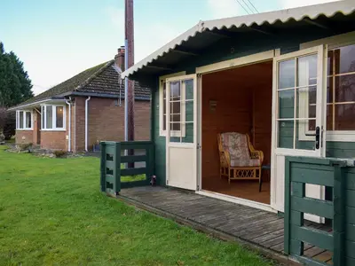 a green house with a porch and a chair on a lawn at Kinverley in Evenjobb