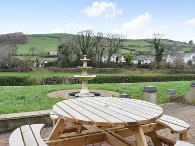 a wooden picnic table with a fountain in a park at Maesbangor Farmhouse in Capel Bangor