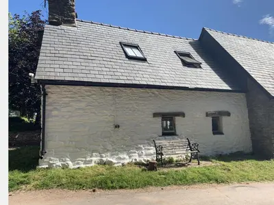 a white building with a bench in front of it at Ty Fferm Hen, Ancient Farmhouse, Coity Bach in Talybont