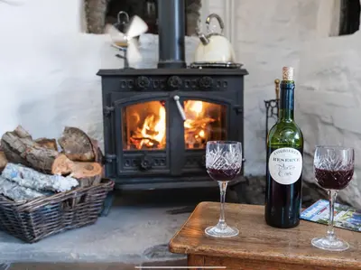 a bottle of wine and two glasses on a table with a fireplace at Ty Fferm Hen, Ancient Farmhouse, Coity Bach in Talybont