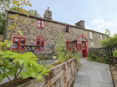 an old stone house with red windows and a garden at Bwthyn Dyfi in Machynlleth