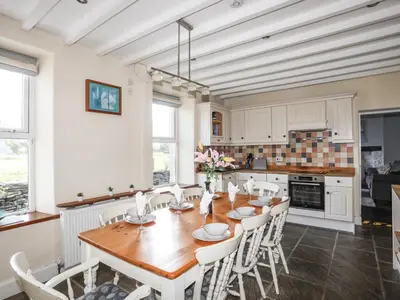 a kitchen with a wooden table and white cabinets at Glyn Morfa in Harlech