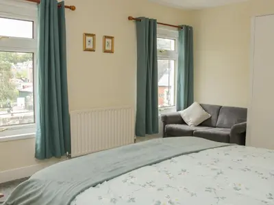 a bedroom with a bed and a chair and windows at Whitewater Cottage in Llangollen