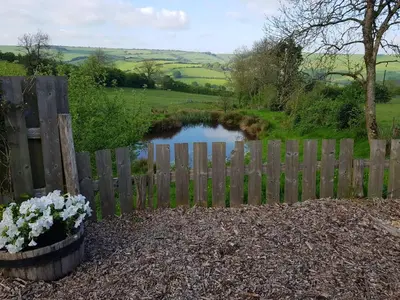 a wooden fence with a small pond behind it at Cornflour Cozy Cabin Retreat in Craven Arms