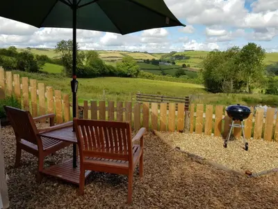 a grill and two chairs with an umbrella and a bbq at Cozy Cabin Retreat - Sleeps 2 & a Child in Craven Arms