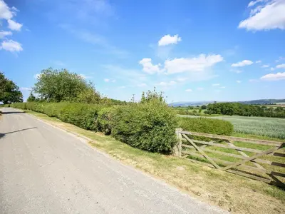 a dirt road with a fence on the side of a field at Norton Cottage in Craven Arms