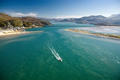 a boat in the water next to a beach at Lovely Large home 10 Minute Walk to Barmouth Beach in Barmouth