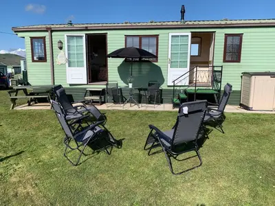 a group of chairs and an umbrella in front of a house at 157 Amour Caravan in Tywyn