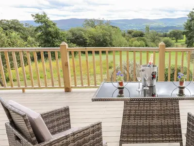 a patio with a table and chairs on a deck at Meadow Lodge in Corwen