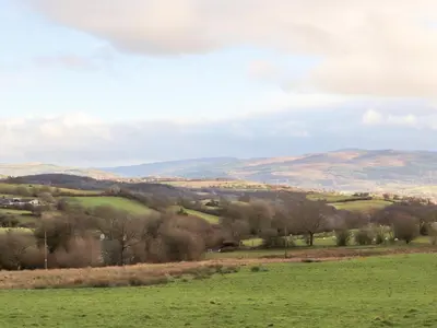 a green field with trees and mountains in the background at Meadow Lodge in Corwen