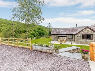 a stone cottage with a wooden fence and a yard at Cwm Dulas in Llanddewi-Brefi