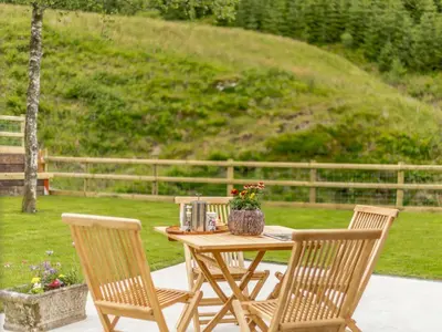 a wooden table with two chairs and a table with flowers at Cwm Dulas in Llanddewi-Brefi