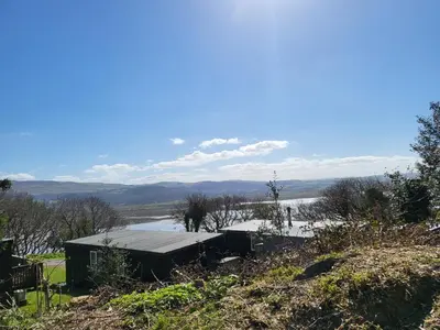 a building on a hill next to a body of water at Foxs Lair Aberdovey in Aberdyfi