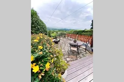 a deck with a table and chairs and flowers at The Little Boat House in Talsarnau