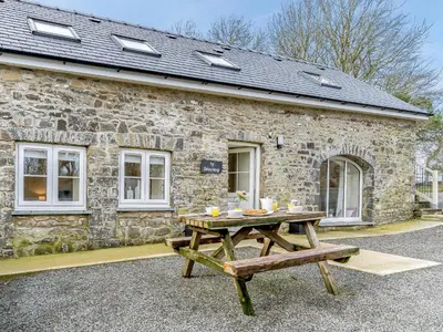 a wooden picnic table in front of a stone building at Ty Draenog - Uk31653 in New Quay