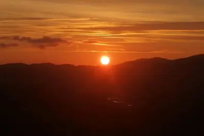 a sunset with the sun setting over the mountains at Bwthyn Gweilch in Machynlleth