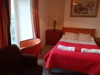 a bedroom with a bed with a red blanket and a chair at Bryncarnedd Farmhouse in Aberystwyth