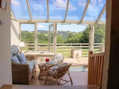 a conservatory with chairs and a table and a window at Brynlikky Cottage in Bucknell