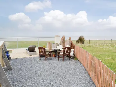 a patio with a table and chairs and the ocean at Plas Bach in Llanon