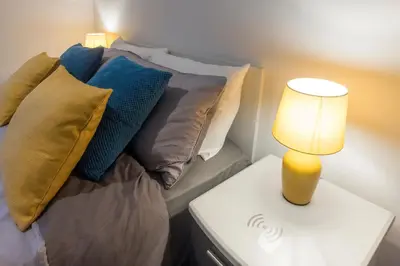 a bed with pillows and a lamp on a table at New central seafront apartment- stunning sea views in Aberystwyth