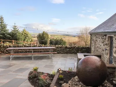a patio with two benches and a stone wall at Drovers Barn in Corwen