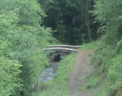 a bridge on a dirt road next to a river at Merlin Cottages in Llandovery