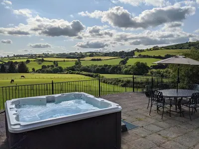 a hot tub on a patio with a table and an umbrella at Caecrwn in Brecon