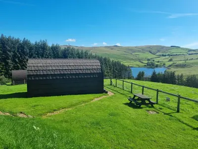 a bench in a field next to a fence and a lake at Forester's Retreat Glamping - Cambrian View- Vaccinated dogs over the age of 2 are accepted in Aberystwyth